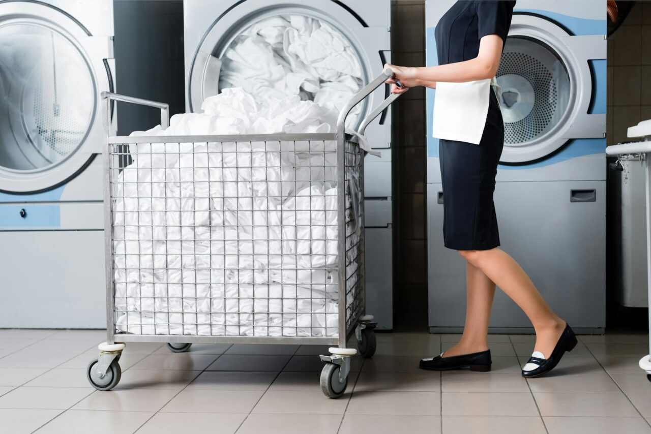 cropped view of housemaid standing near cart with bedding in laundry